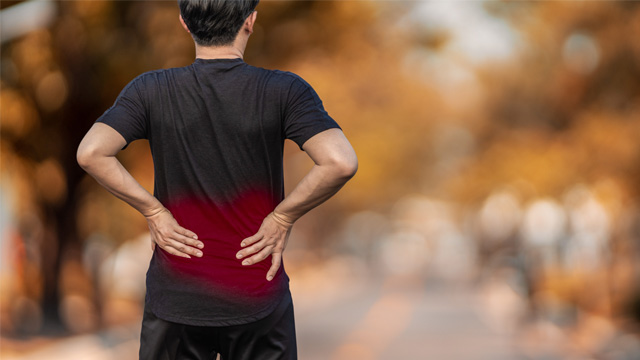 Man standing and holding lower back with both hands as in pain. 